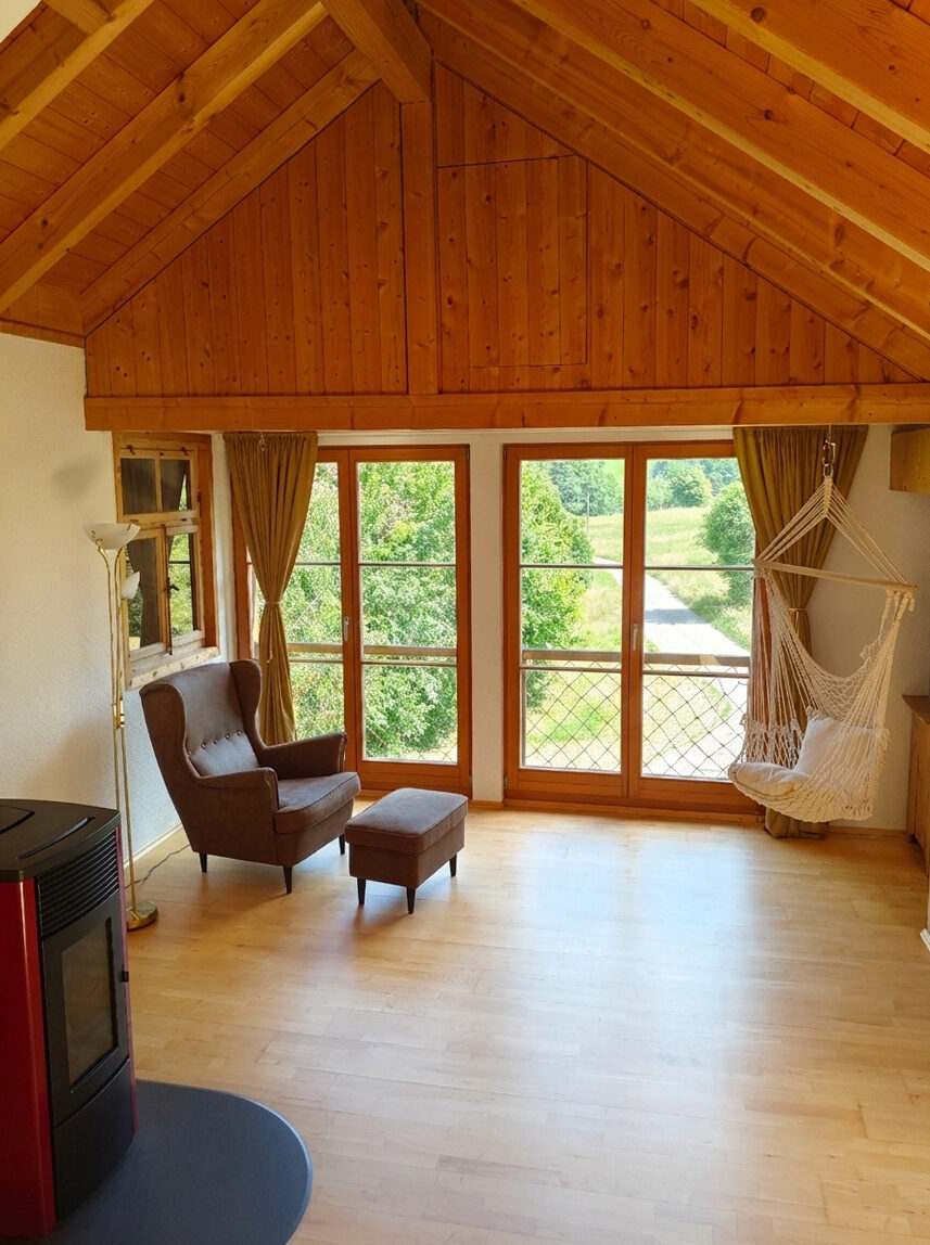 Wohnbereich mit Blick unters Dachgebälk, Hängesessel, Ohrensessel und großen Fenstern im Chalet-Loft Wutachblick